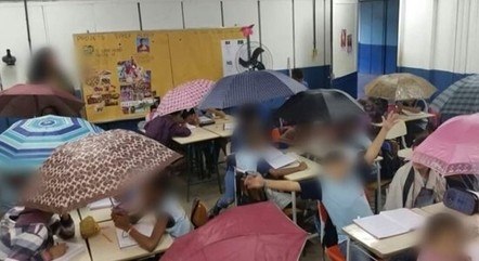 Alunos usam guarda-chuvas para se proteger de goteiras e poder assistir aula em escola